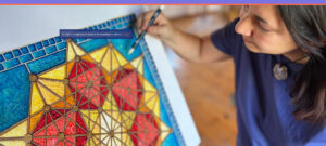 Kristen Palana painting a geometric mandala in bright blue, yellow, and red—closeup of art and artist’s hand.